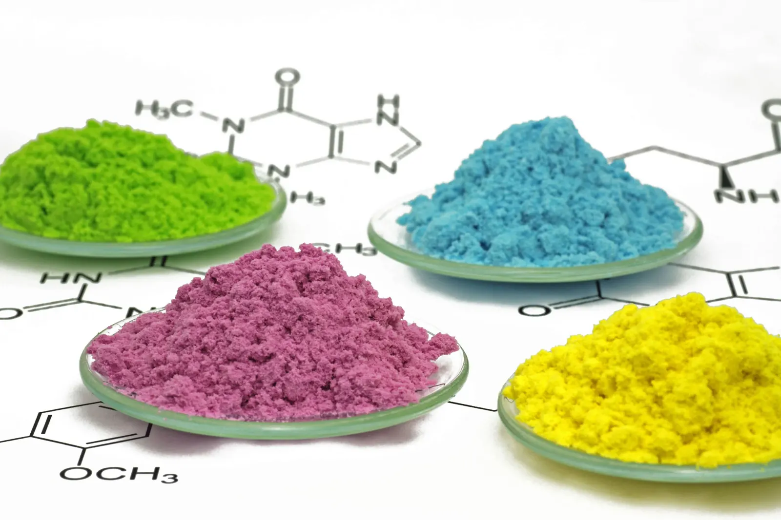 Green, blue, magenta and yellow pigment powders weighed out in laboratory dishes